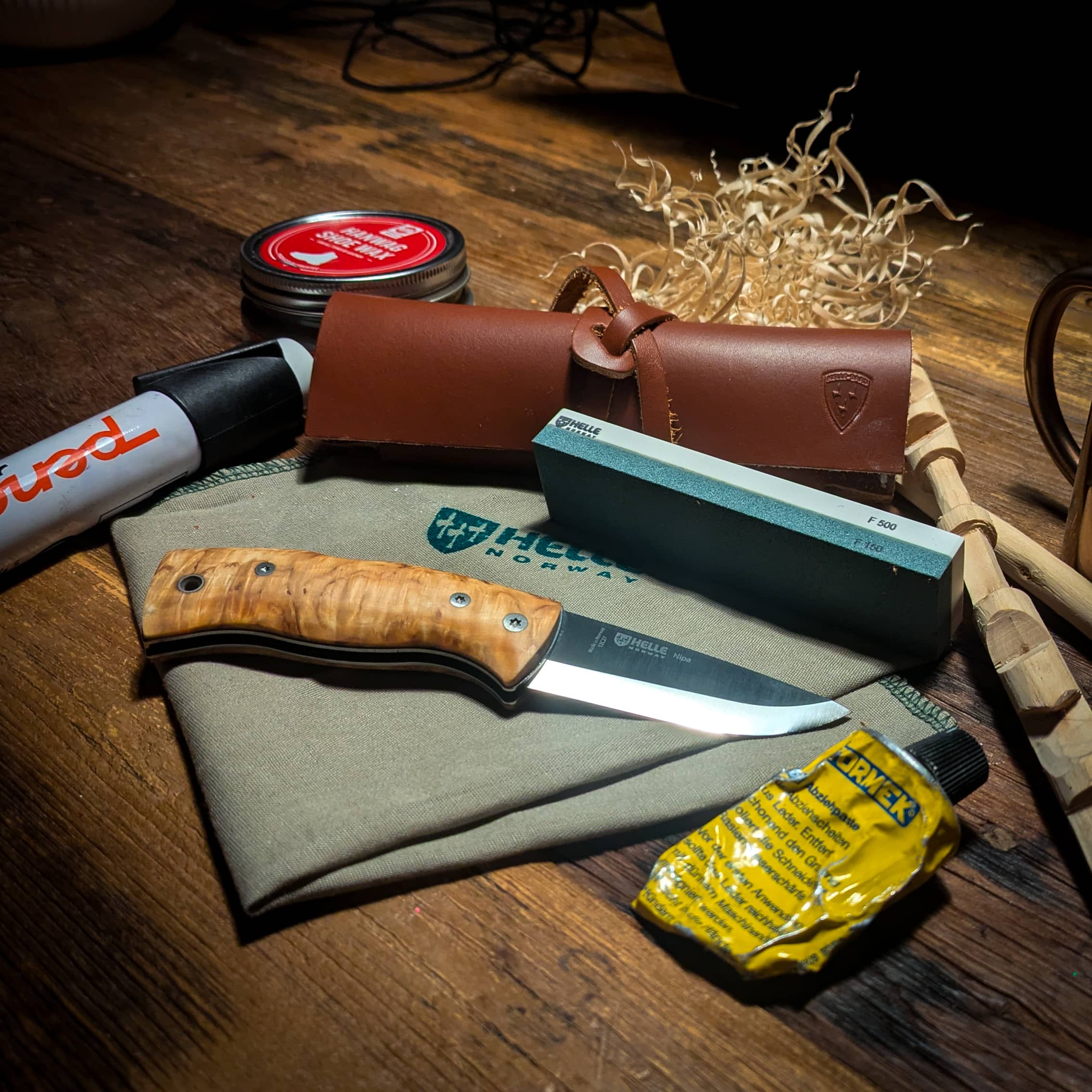 Helle Nipa knife beside a Helle sharpening stone, leather strop and honing compound on a wooden table