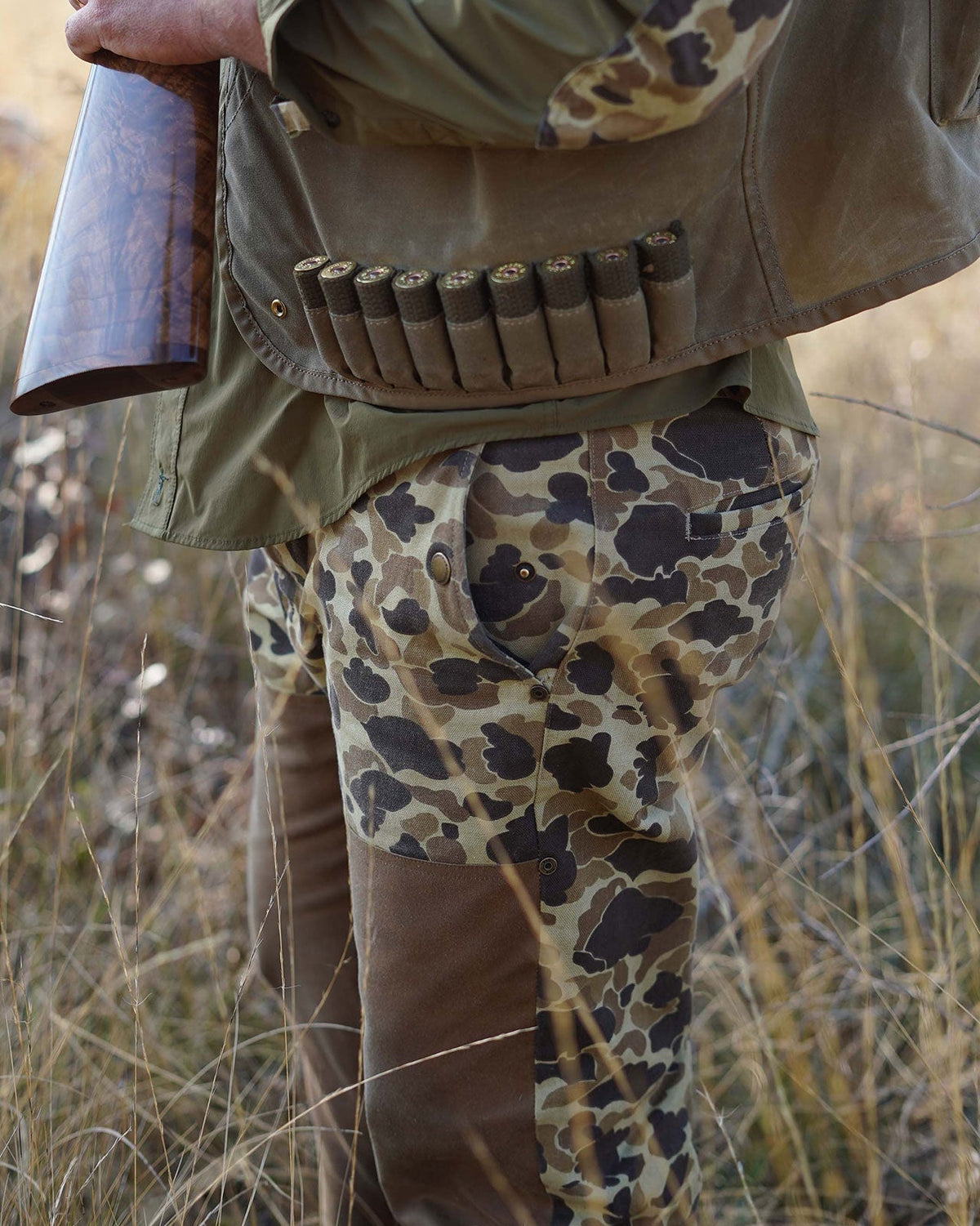 Hunter wearing the Original Camo Midweight Field Pant with a shell belt in tall grass