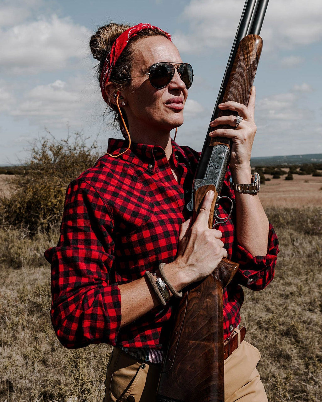 Woman in sunglasses holding a shotgun while wearing the red Mini Buffalo Plaid Joan Shirt