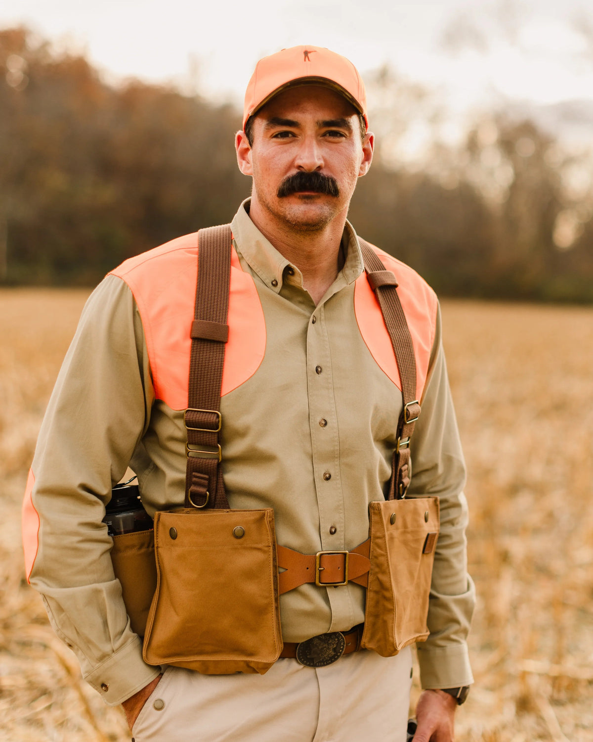 Upland hunter in a blaze orange cap wearing the Signature Canvas Strap Vest in a harvested field