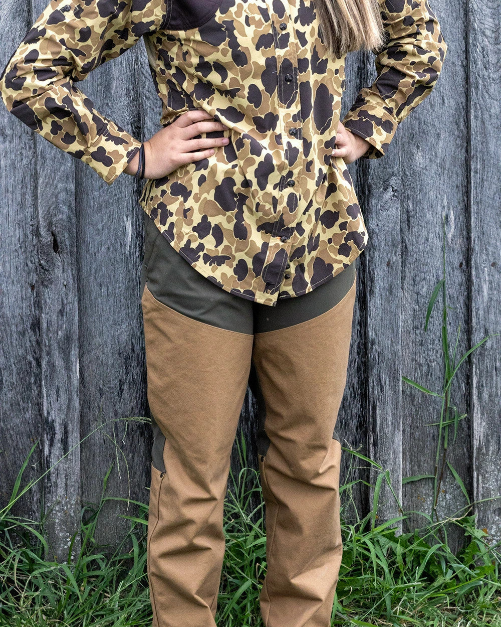 Woman in an Original Camo shirt wearing the Loden Active+ Joan Field Pant at a fence