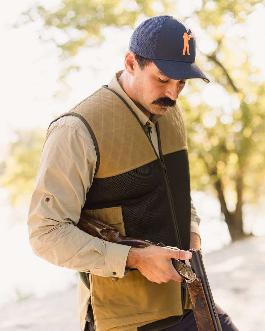 Shooter in a navy cap wearing the Heritage Clays Vest and loading an over-under