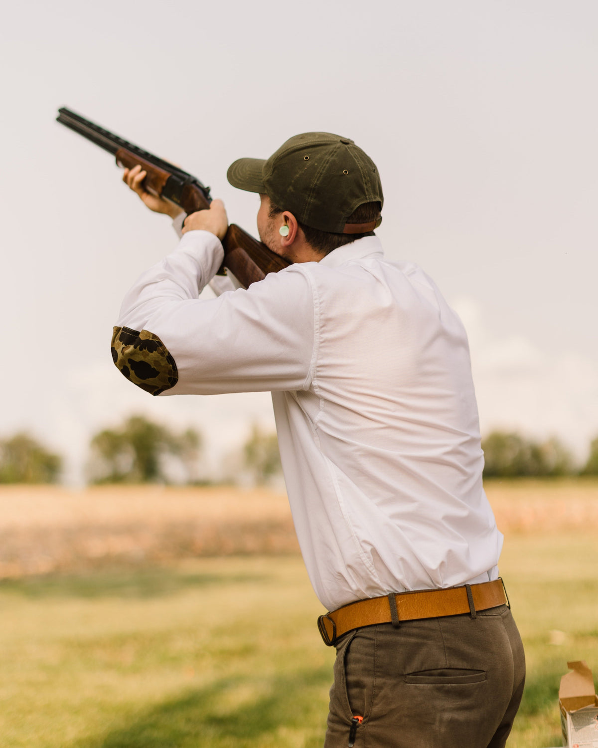 Shooter in the White Oxford Sportsmans Shirt mounting a shotgun on a clays course