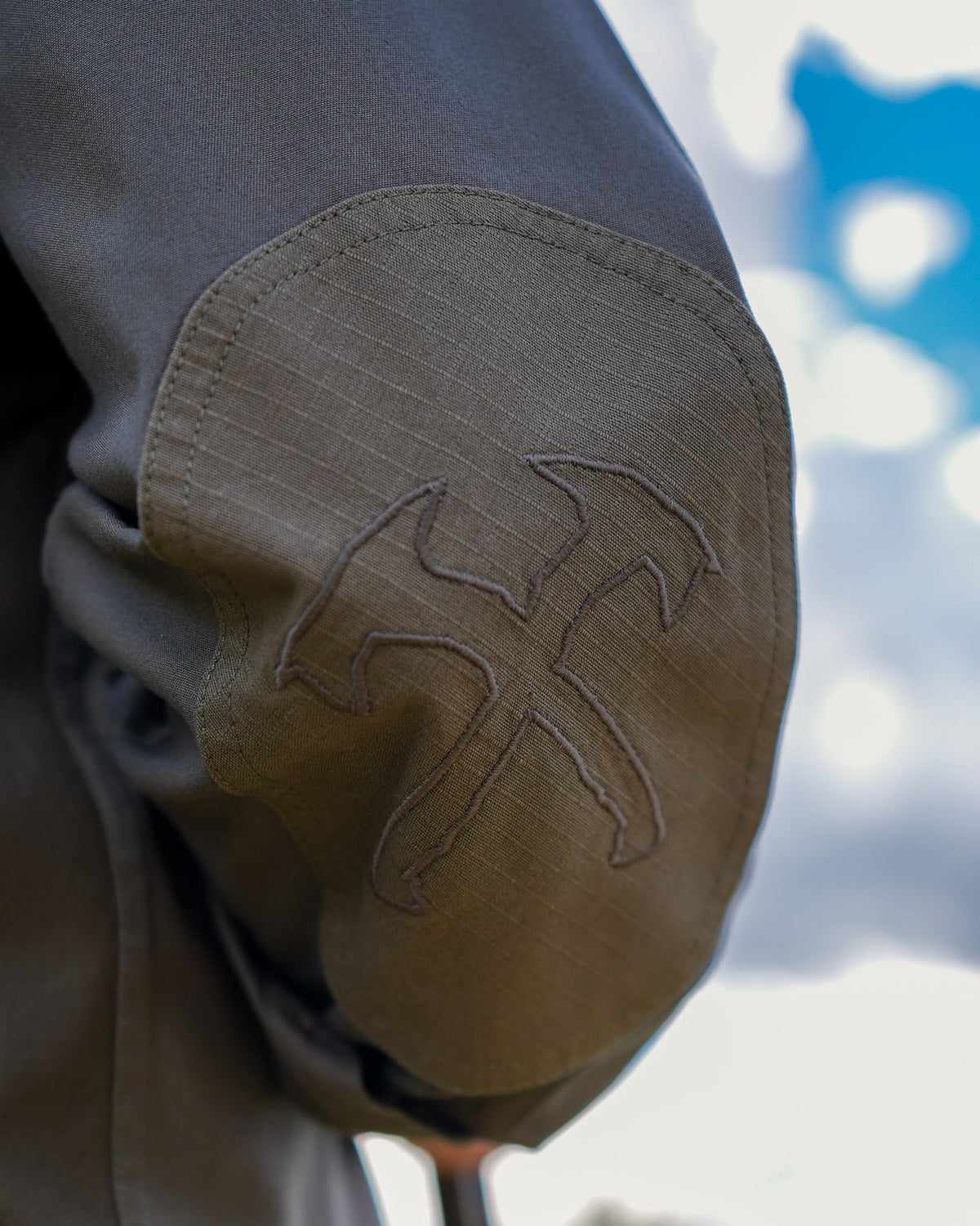 Crossed tomahawks embroidered elbow patch on the Jack Carr Hunters Shirt, worn outdoors