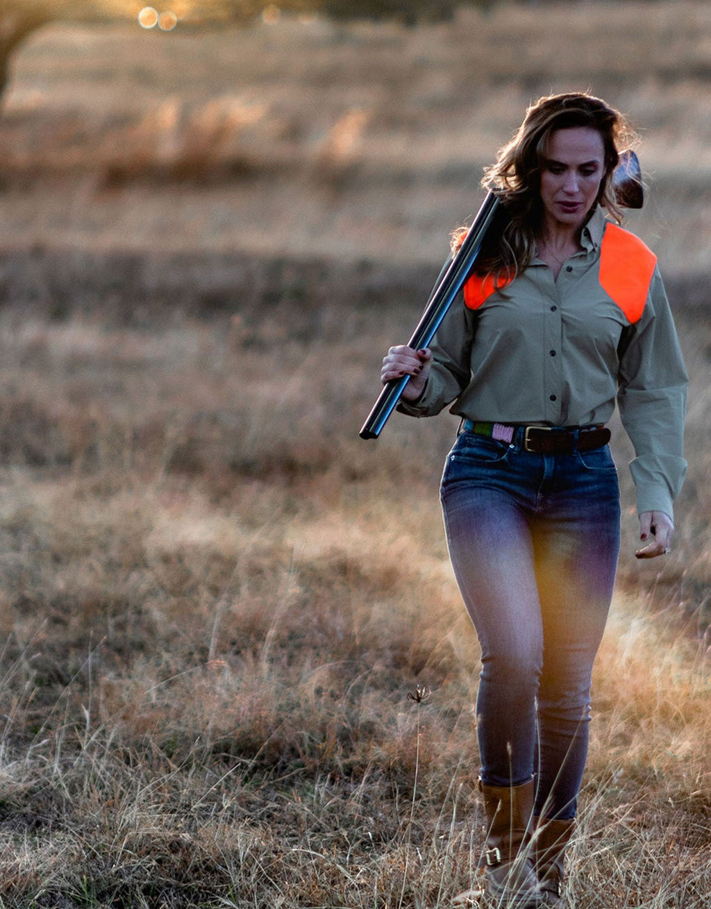 Woman walking a grass field with a shotgun wearing the Active+ Joan Field Shirt in Upland