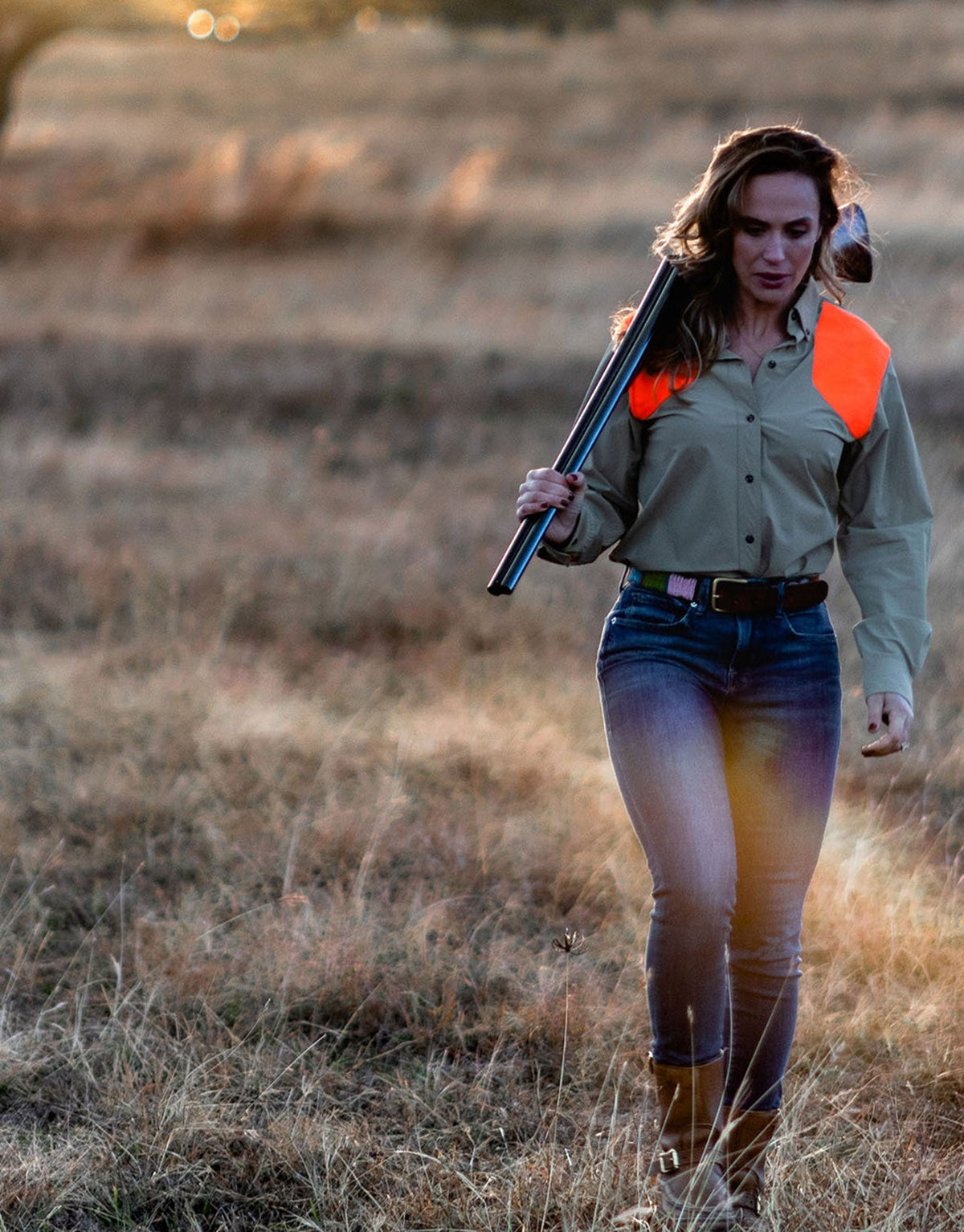 Woman walking a grass field with a shotgun wearing the Active+ Joan Field Shirt in Upland