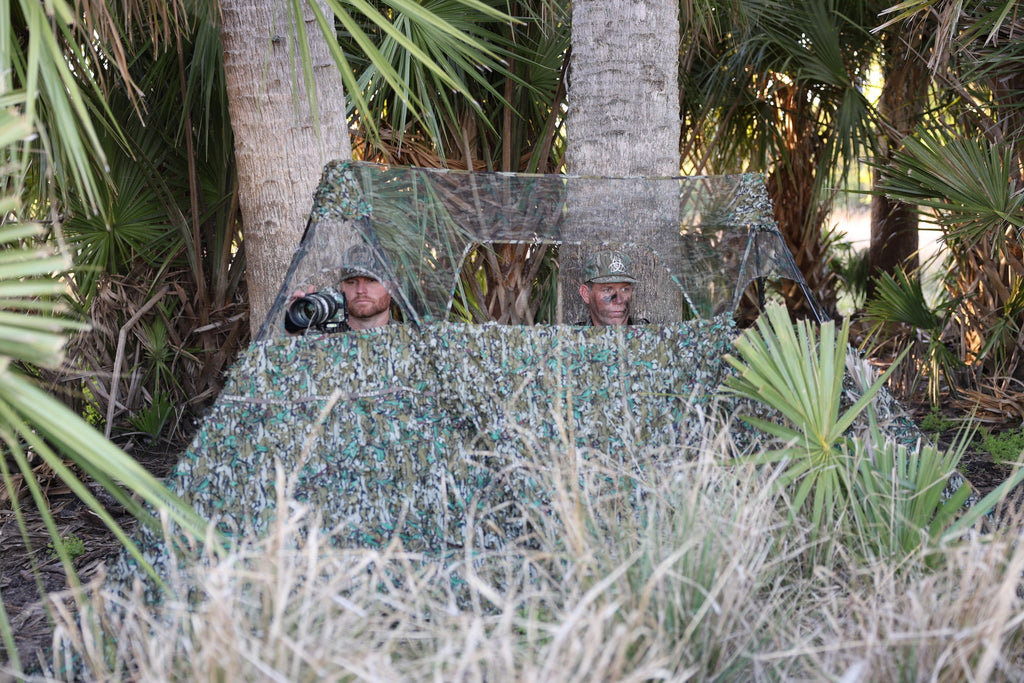 Camouflage hunting blind with mesh windows for wildlife photography in dense palm foliage