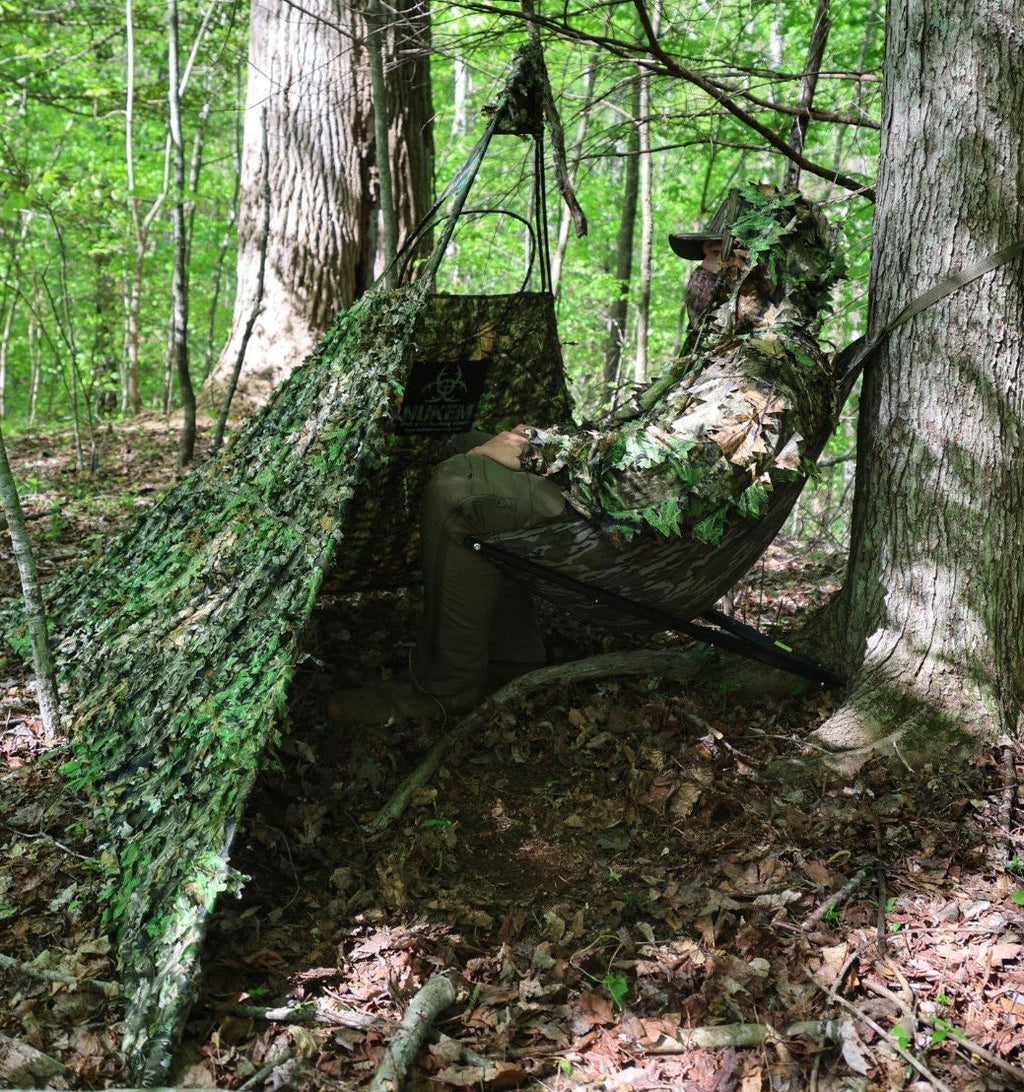 Hunter in leafy ghillie suit using camo hammock blind in forest, ideal for deer hunting and wildlife observation