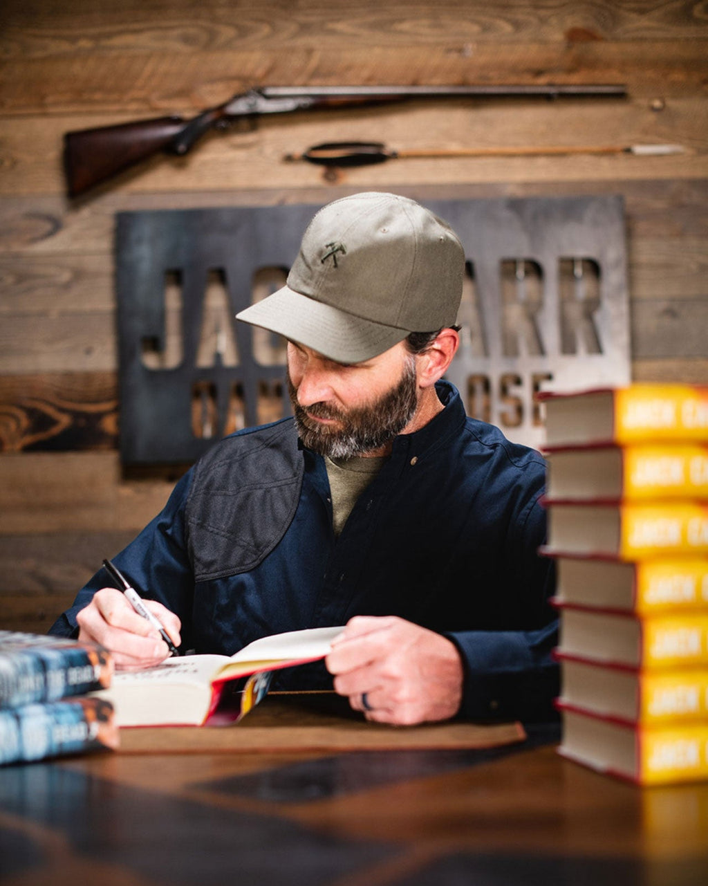 Author Jack Carr signing books at a table wearing a camo cap