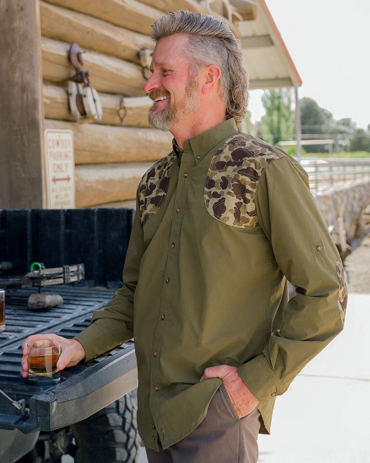 Man in the Olive Active+ Field Shirt standing at a truck tailgate outside a cabin