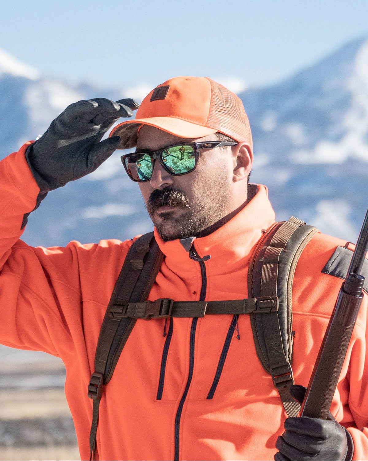 Upland hunter in blaze orange jacket adjusting the blaze orange Arthur Snapback in the mountains