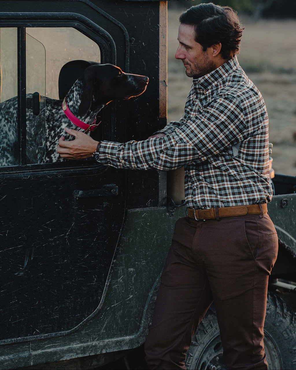 Man in a plaid shirt and Bark Heritage Pant loading a dog into a UTV