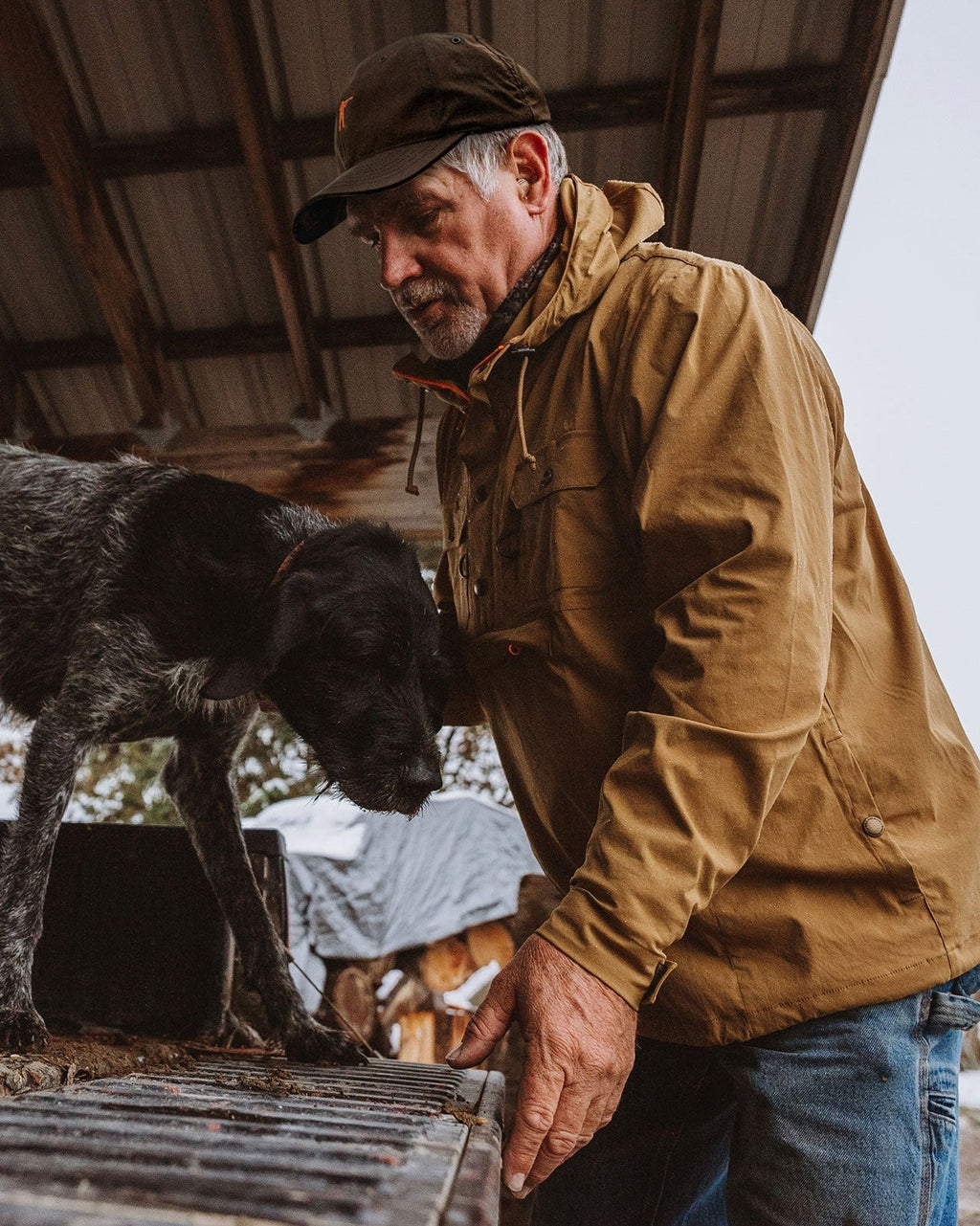 Man wearing the tan Active+ Anorak loading a dog box in a barn