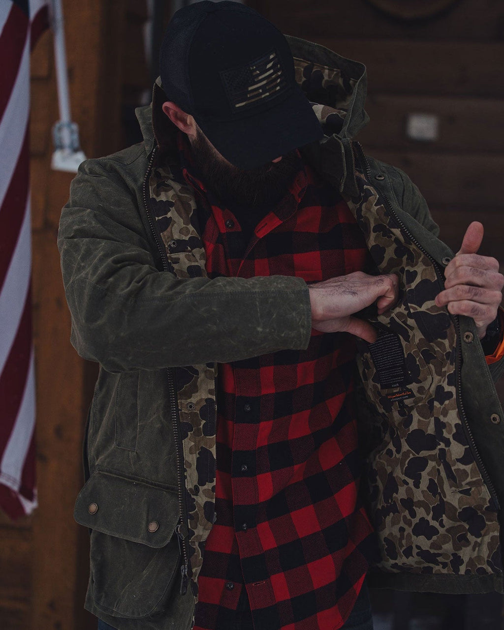 Olive Upland Jacket worn open over a buffalo plaid shirt on a cabin porch