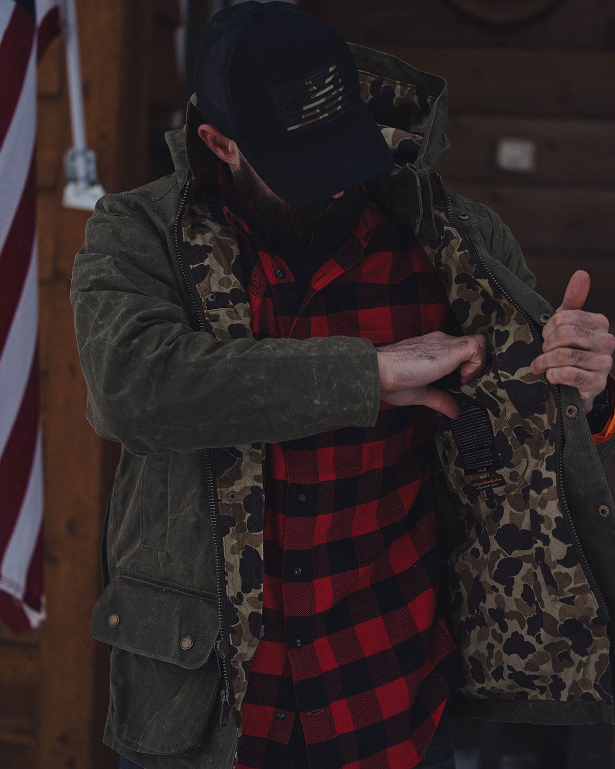 Olive Upland Jacket worn open over a buffalo plaid shirt on a cabin porch