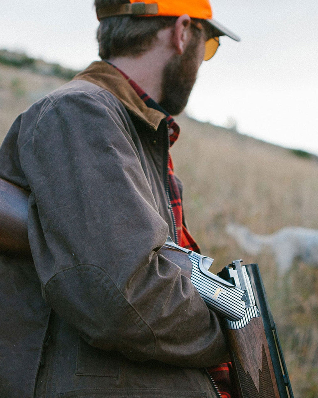 Upland hunter carrying a shotgun wearing the Dark Oak Upland Jacket and blaze orange cap