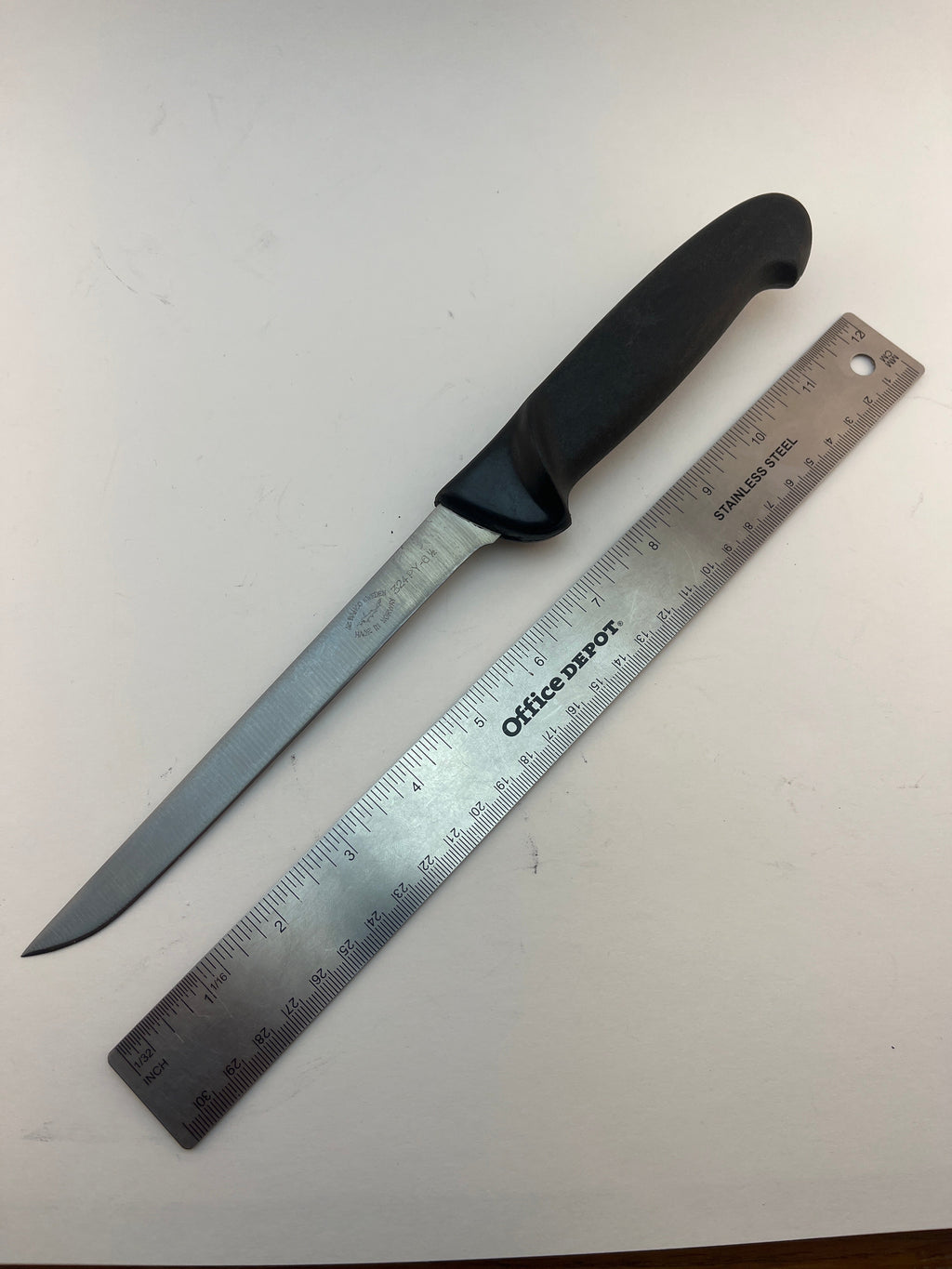 Stainless steel hunting knife with black handle, shown next to ruler for scale
