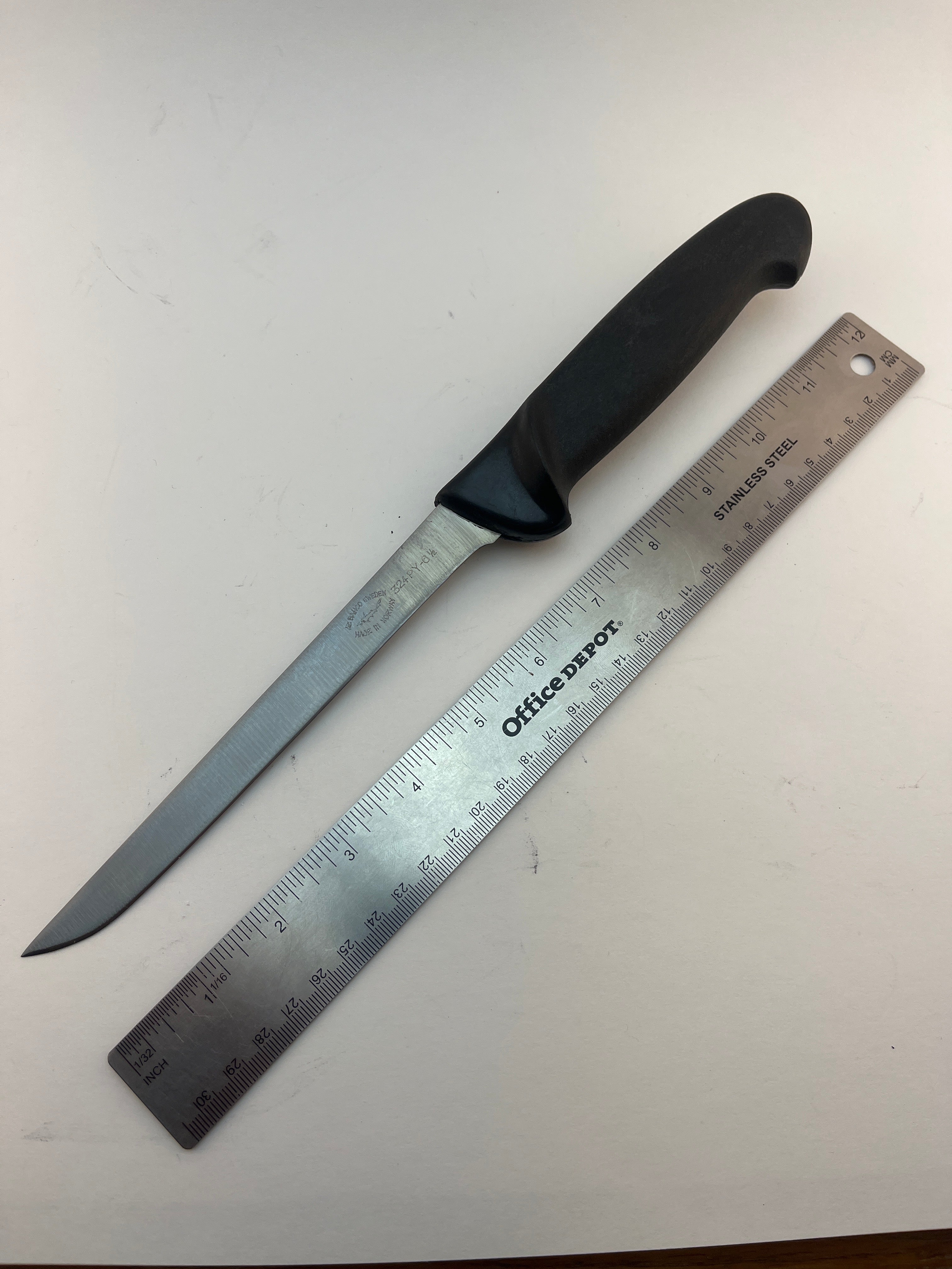 Stainless steel hunting knife with black handle, shown next to ruler for scale