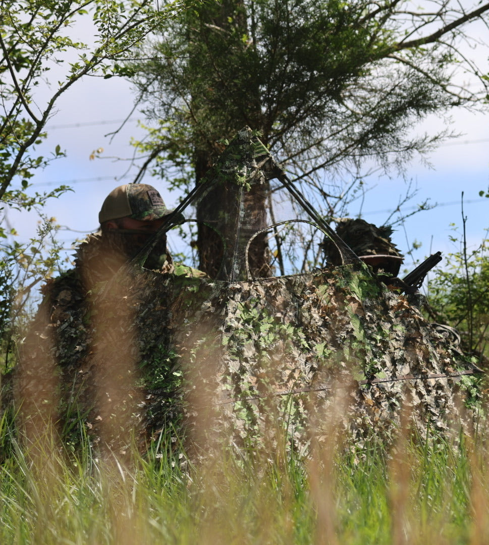 Hunting blind with leafy camouflage netting for outdoor concealment in woods