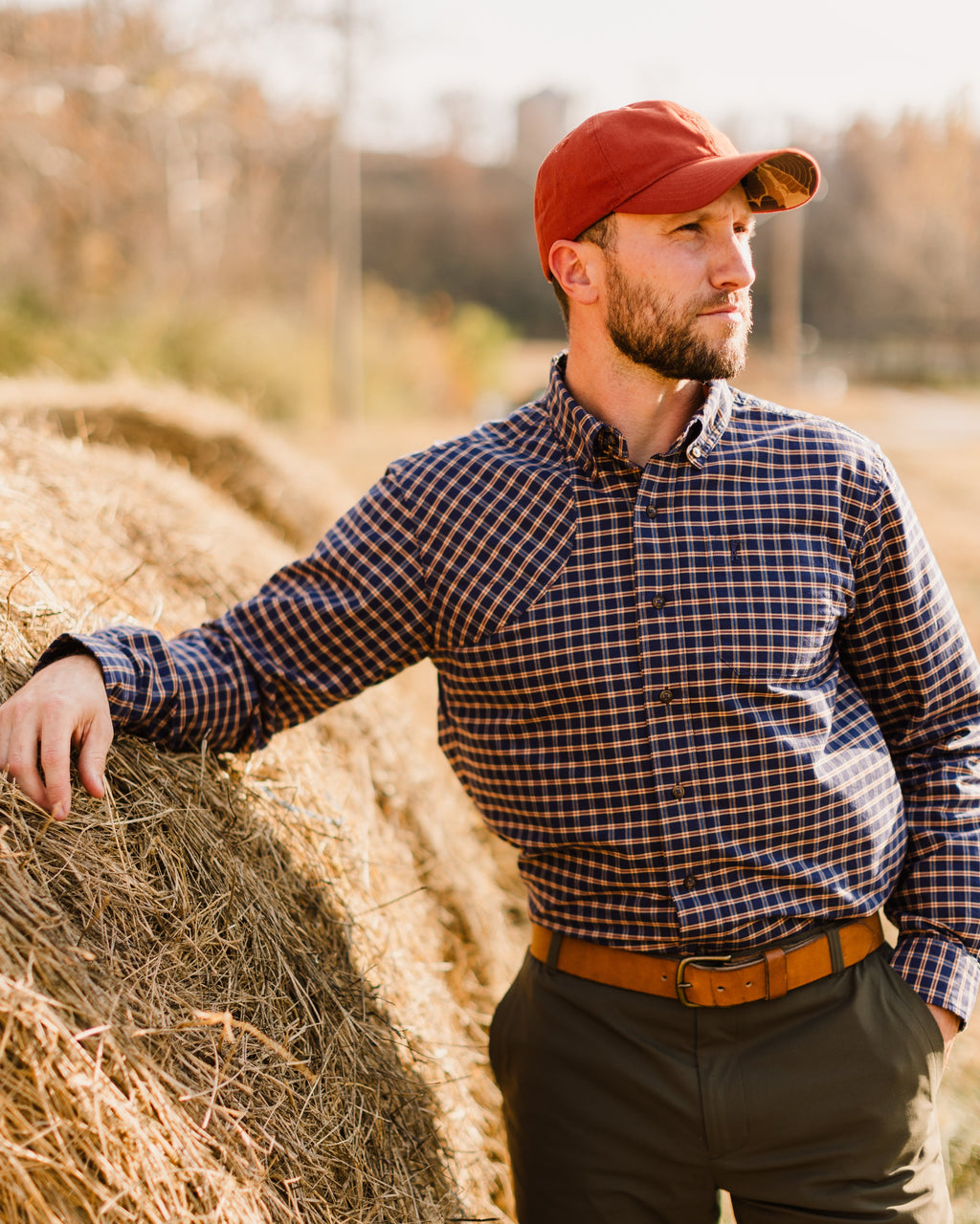 Man leaning on a round hay bale wearing the Burnt Orange Arthur Core Hat