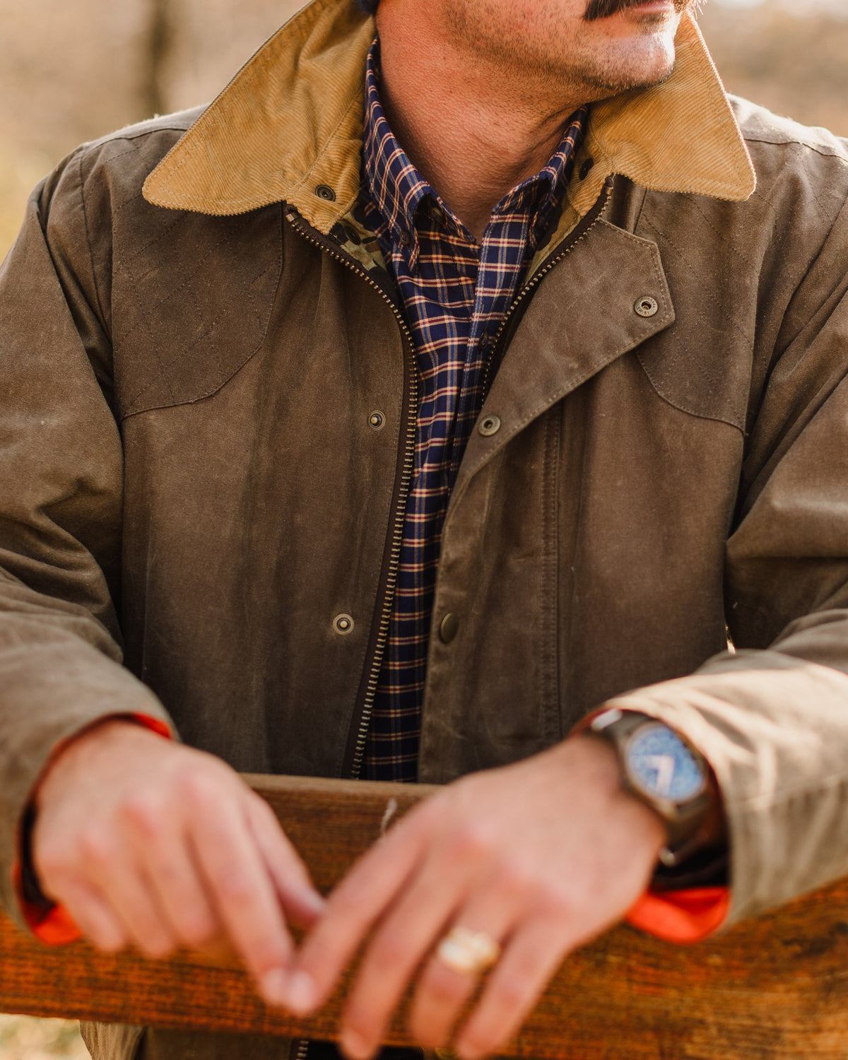 Close-up of hands resting on a rail, man wearing the Olive Upland Jacket