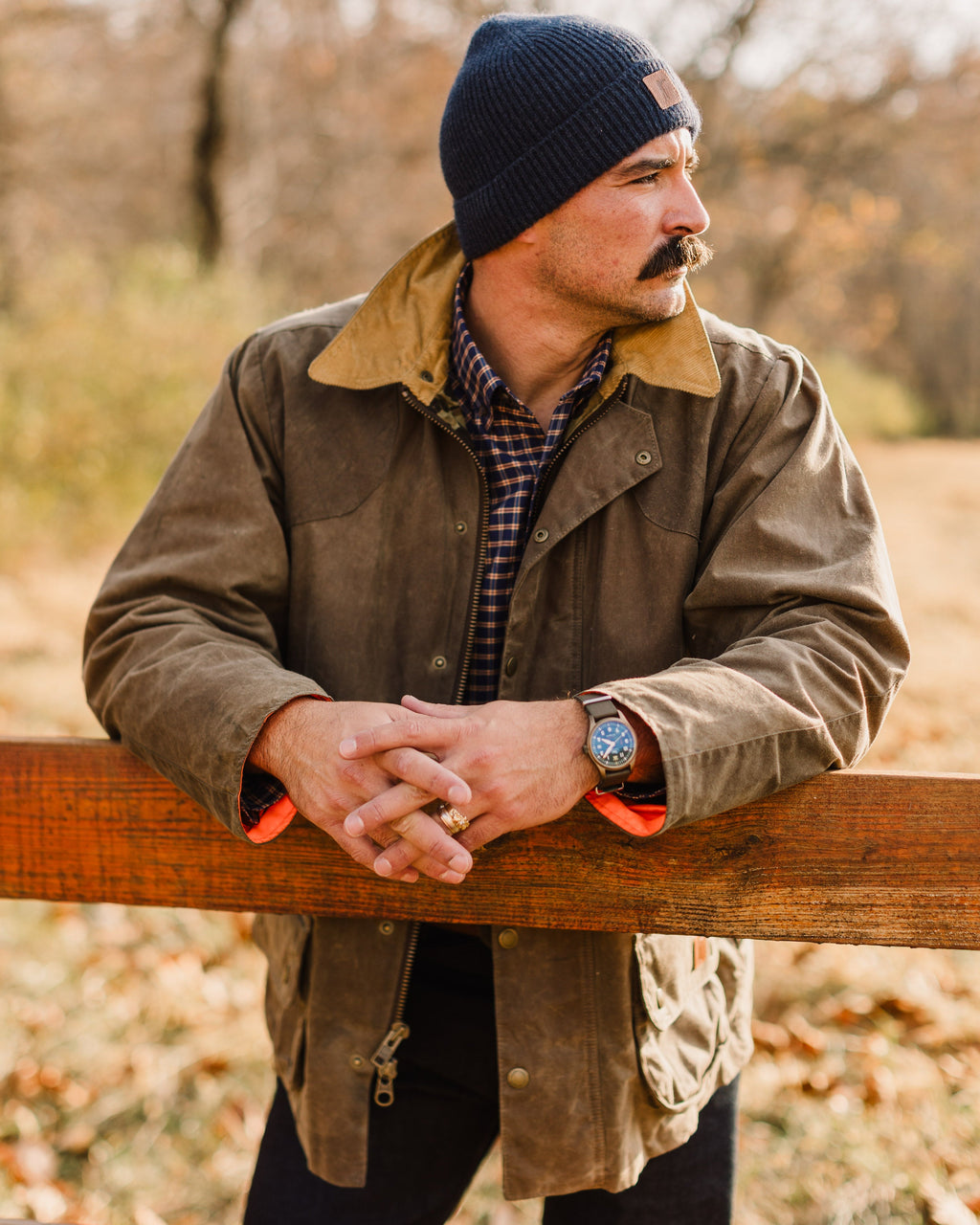 Man in the Olive Upland Jacket leaning on a wooden fence rail