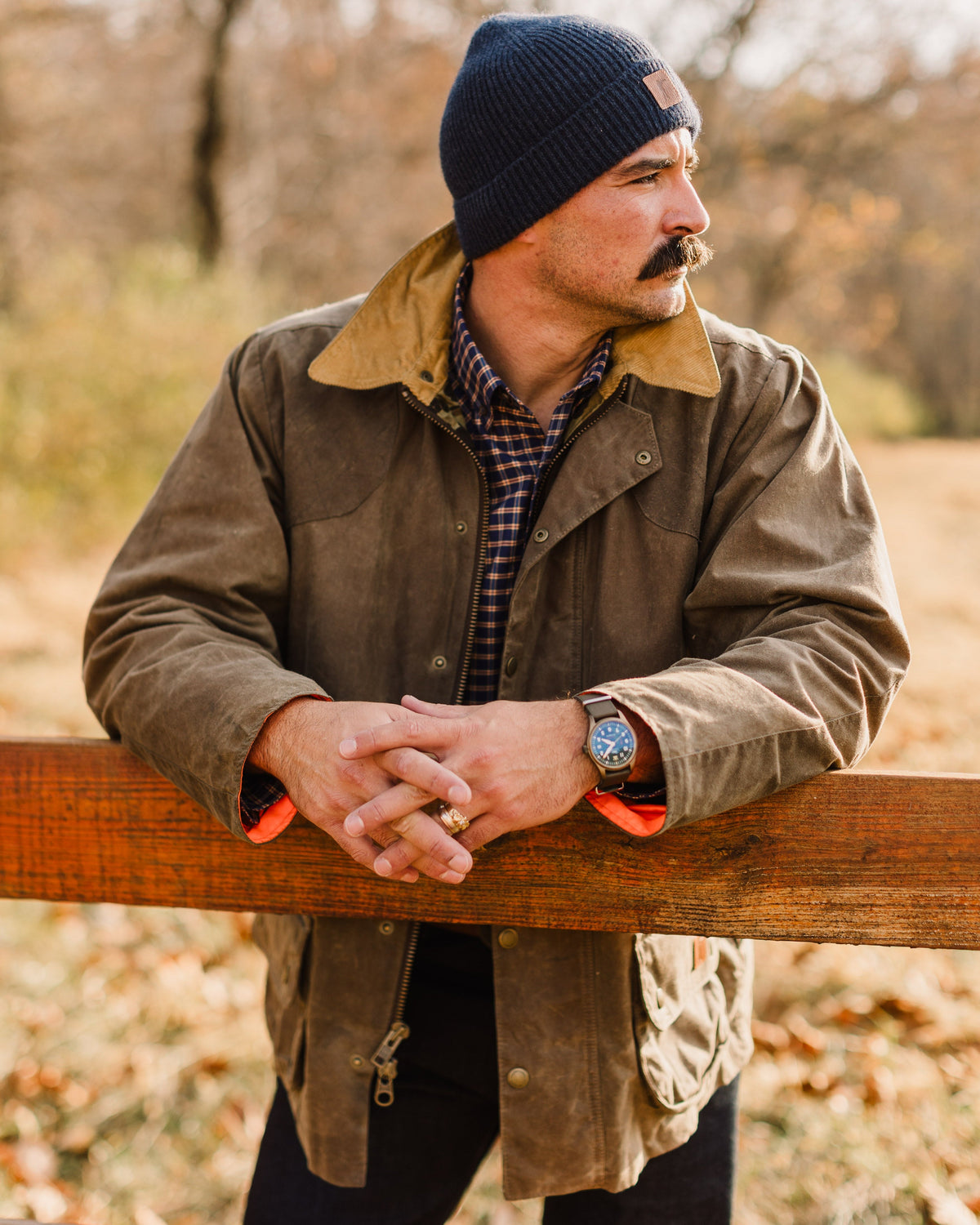 Man in the Olive Upland Jacket leaning on a wooden fence rail