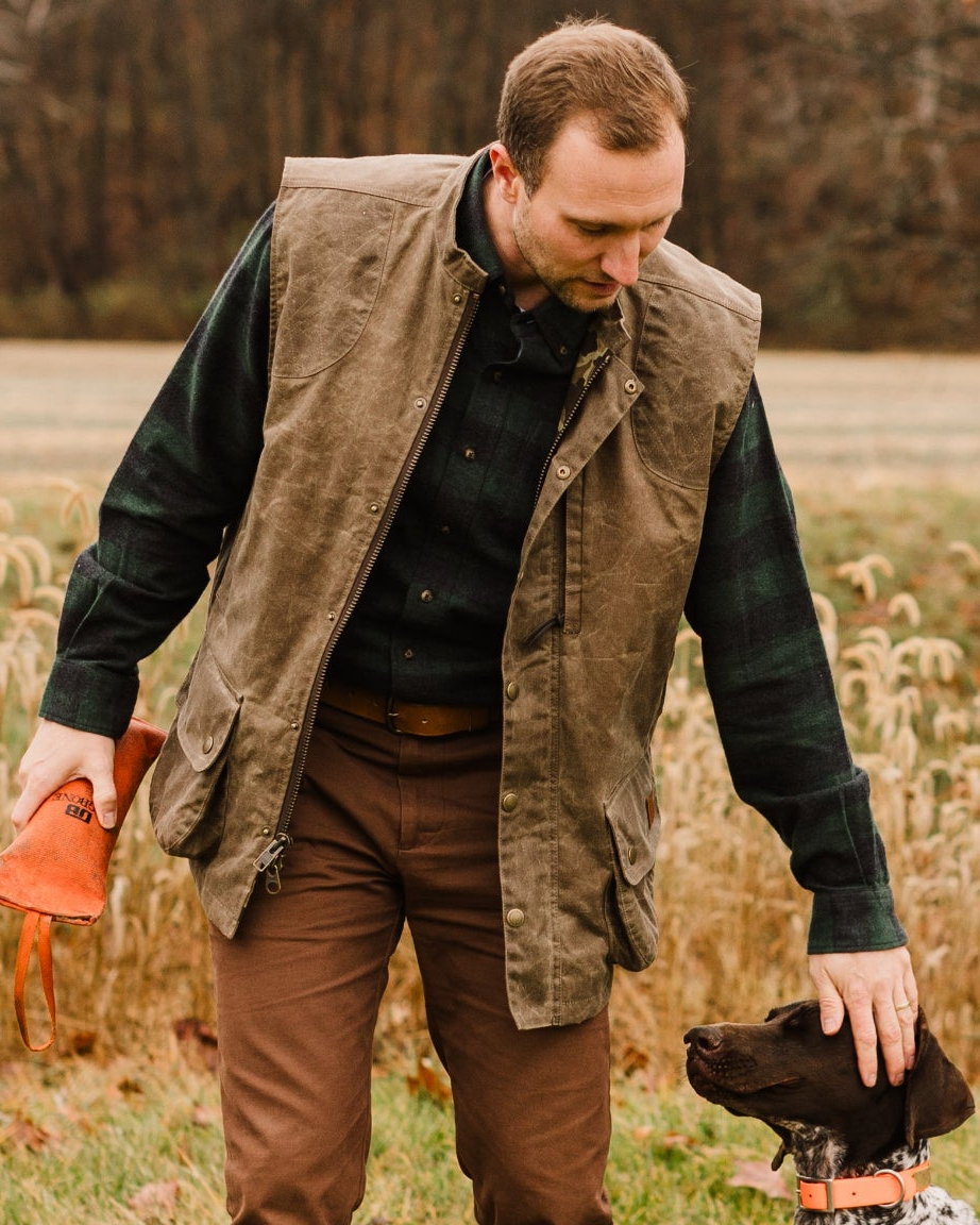 Hunter in the Dark Oak Upland Vest kneeling with a bird dog and an orange training bumper
