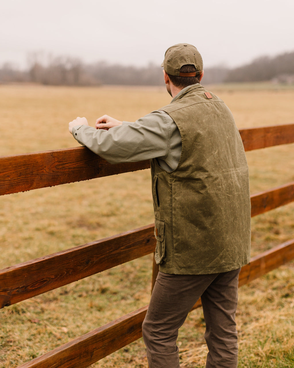 Back of the Olive Upland Vest worn at a wooden fence