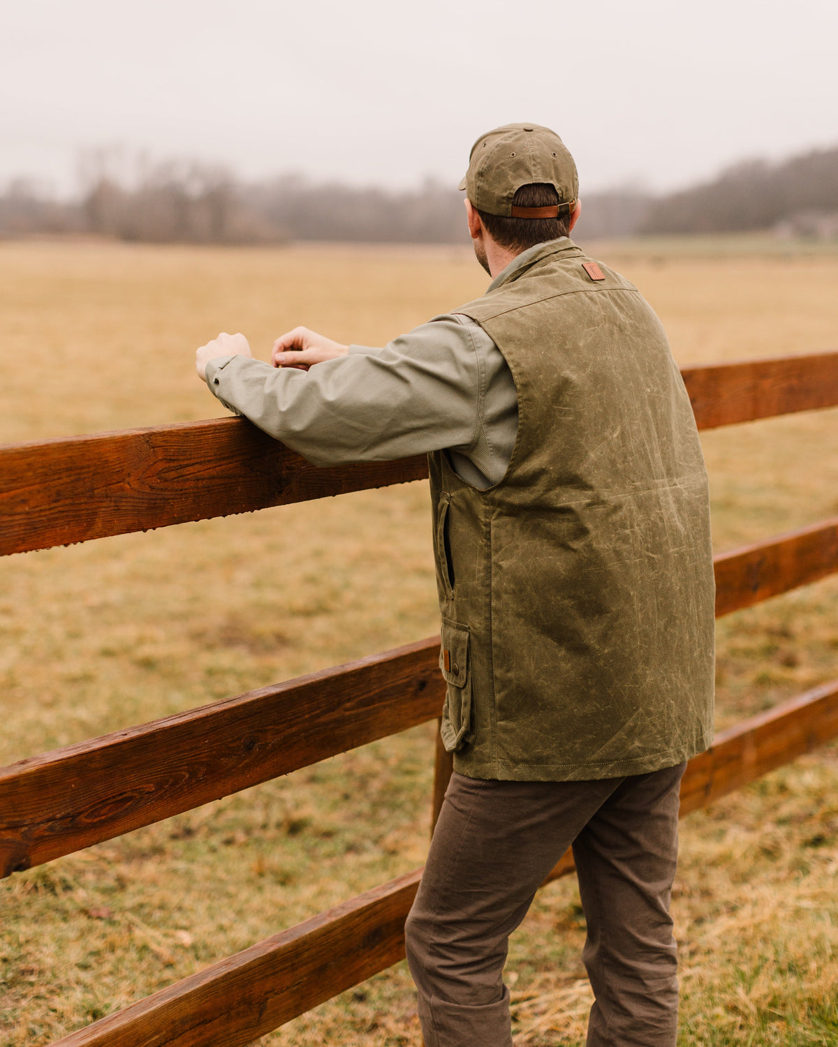 Back of the Olive Upland Vest worn at a wooden fence