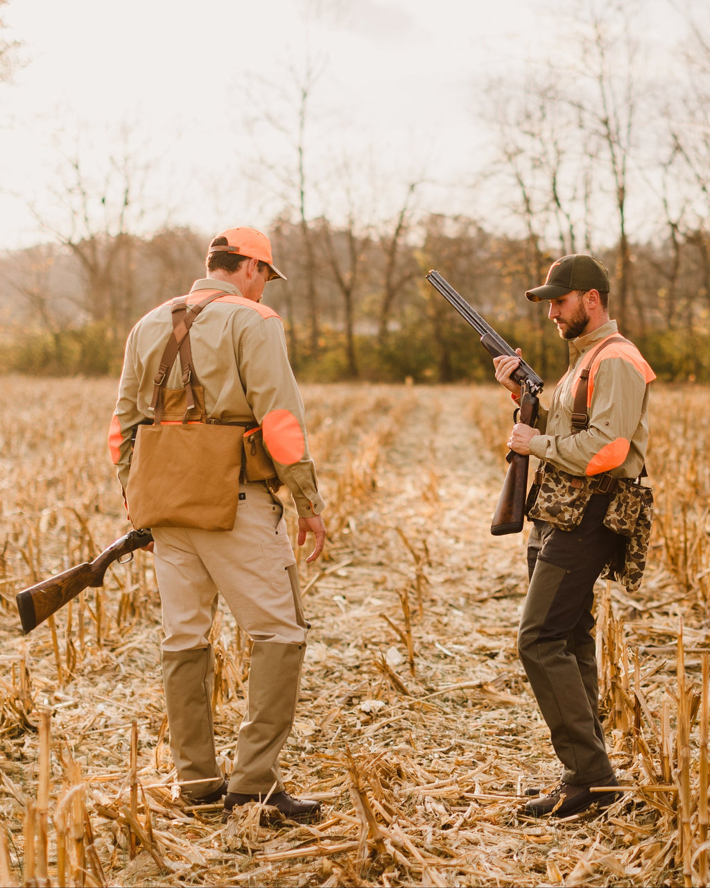Two hunters with shotguns walking a corn field, one wearing the Original Camo Strap Vest