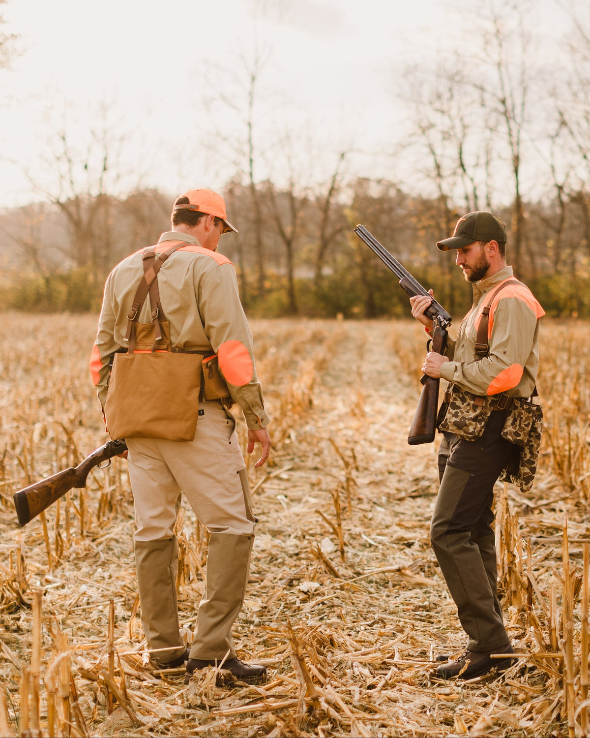 Two hunters with shotguns walking a corn field, one wearing the Original Camo Strap Vest