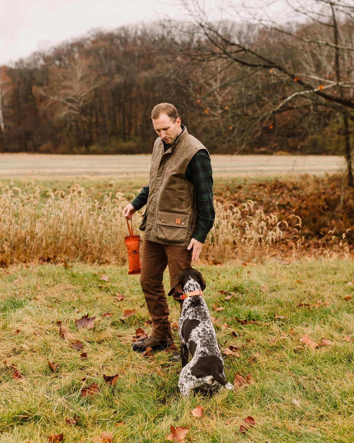 Hunter in the Dark Oak Upland Vest working a bird dog in a cut field