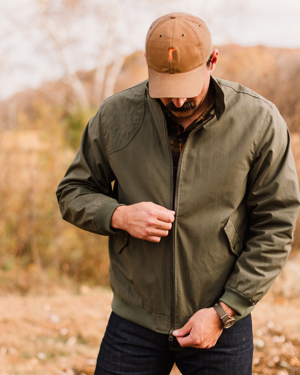 Man looking down while zipping the Sage Green Harrington Jacket