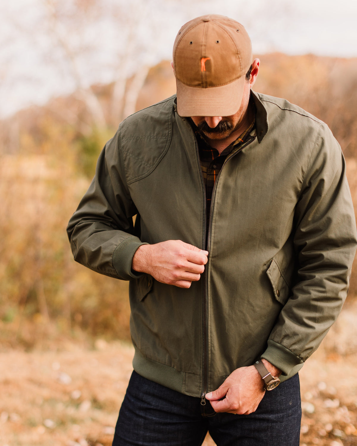 Man looking down while zipping the Sage Green Harrington Jacket