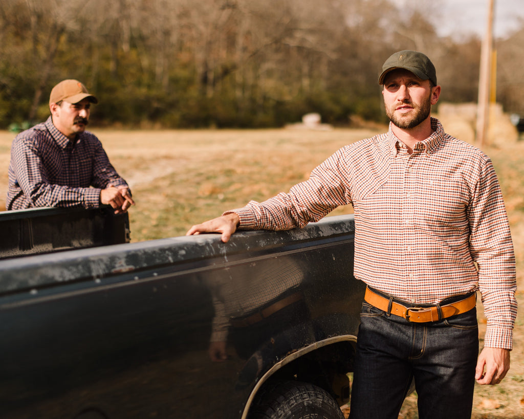 Man in an Olive Arthur Core Hat leaning on a truck tailgate in a field