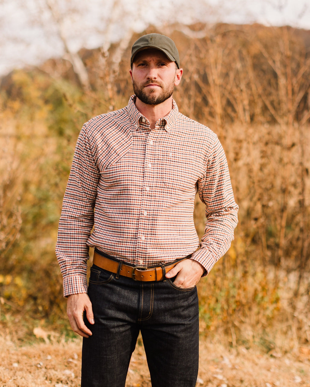 Man wearing the Olive Arthur Core Hat with a check button-down in tall grass
