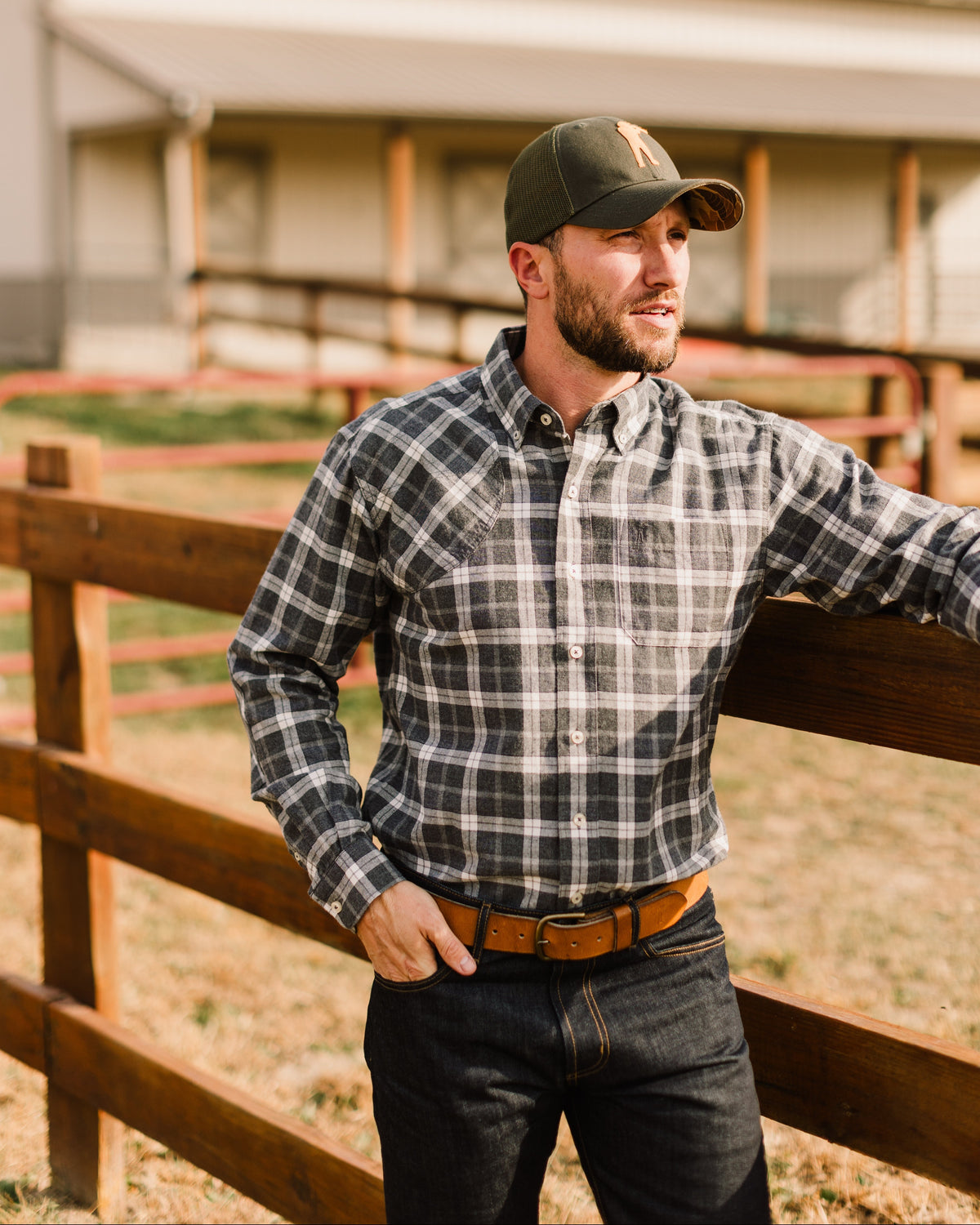 Man in a plaid flannel and the Olive Arthur Core Snapback at a wooden fence