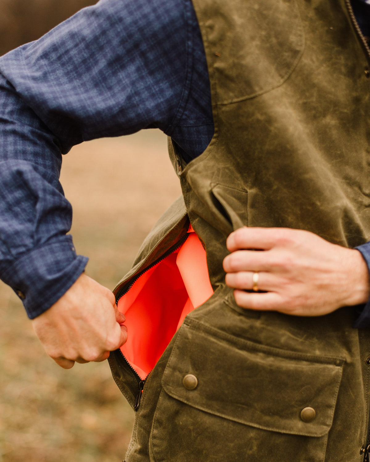 Hand opening the blaze orange lined side game pocket on the Olive Upland Vest