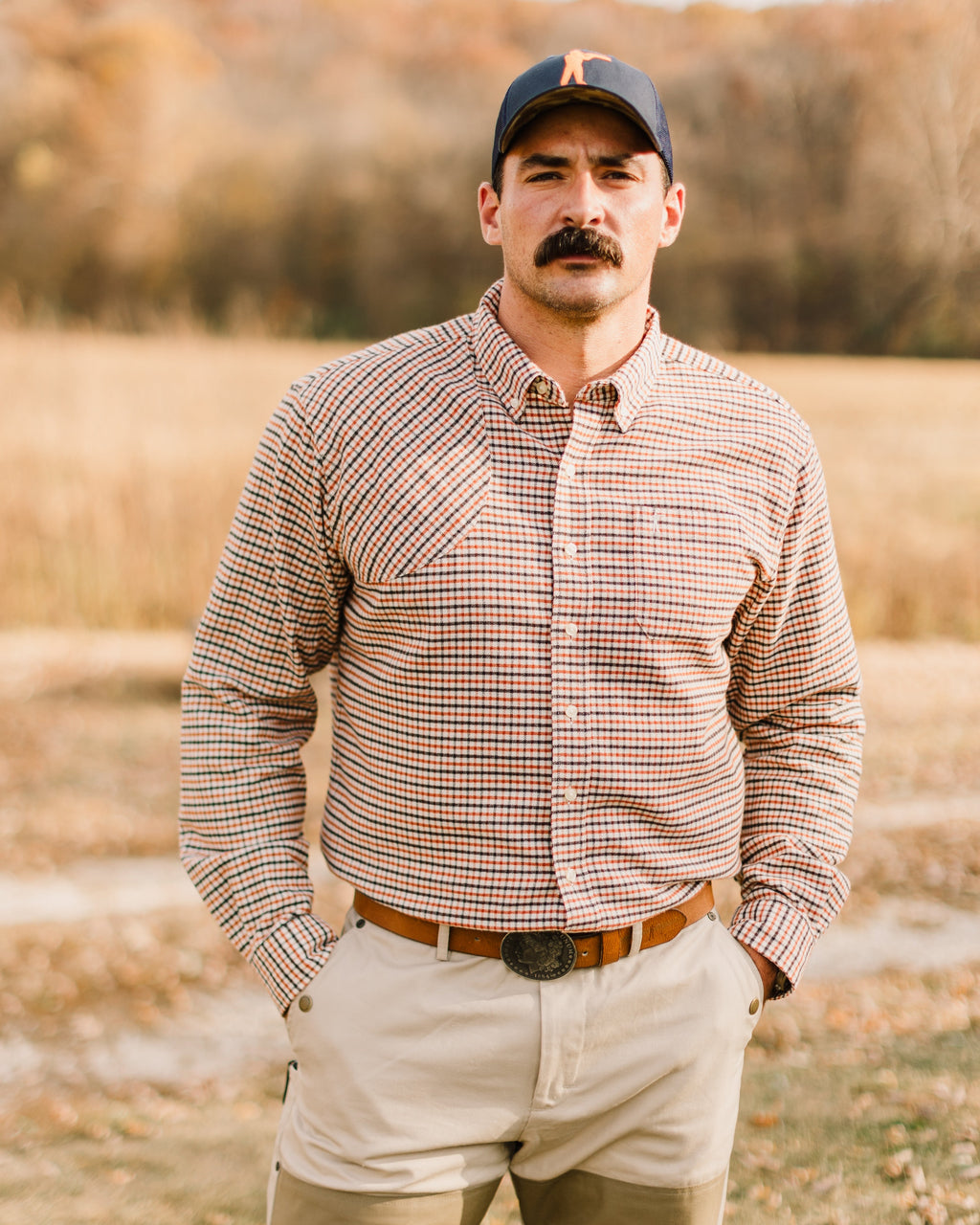 Man in a check shirt and khaki pants wearing the Ball and Buck leather belt in a field