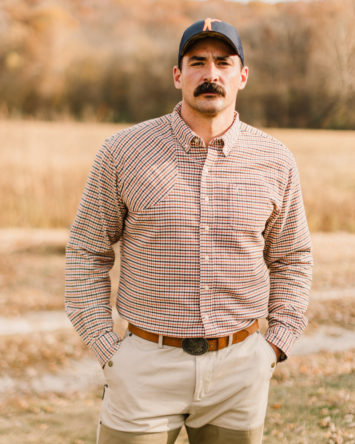 Man in a check shirt and khaki pants wearing the Ball and Buck leather belt in a field