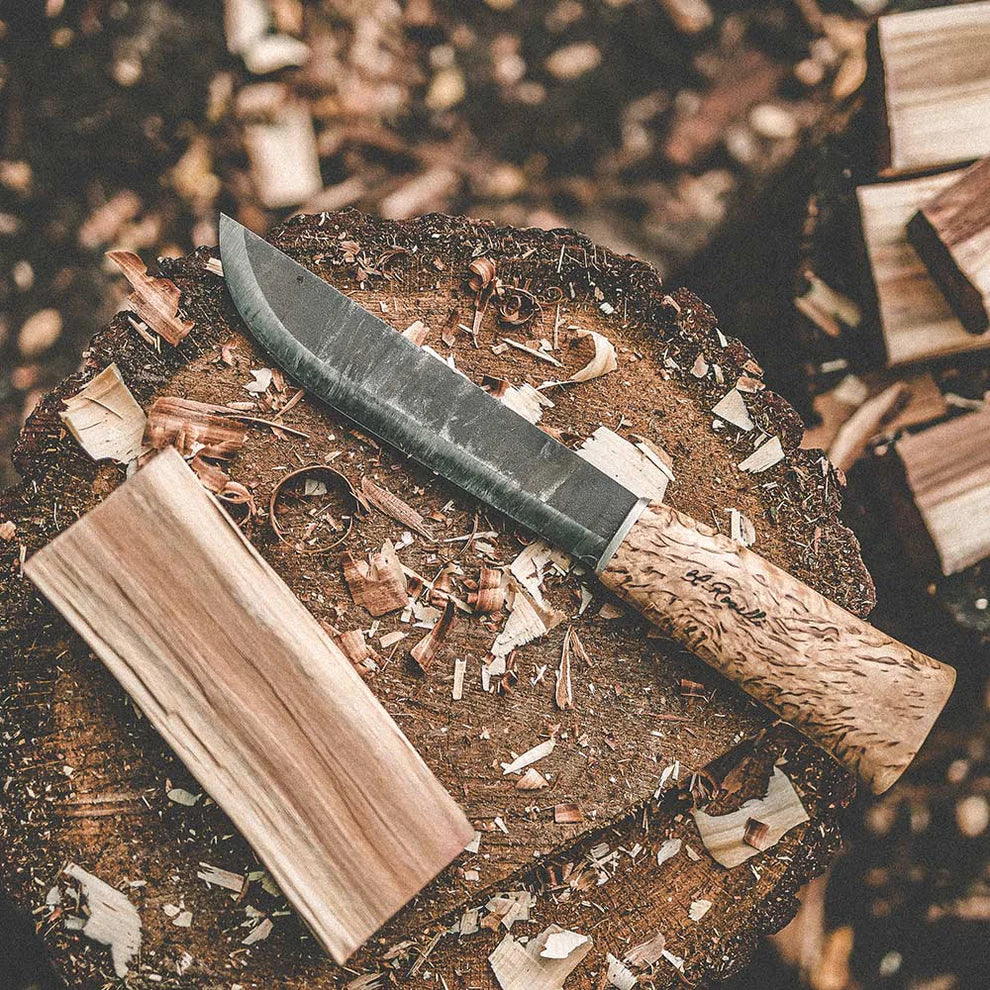 Hand-forged hunting knife with wooden handle on tree stump, ideal for outdoor survival and bushcraft tasks