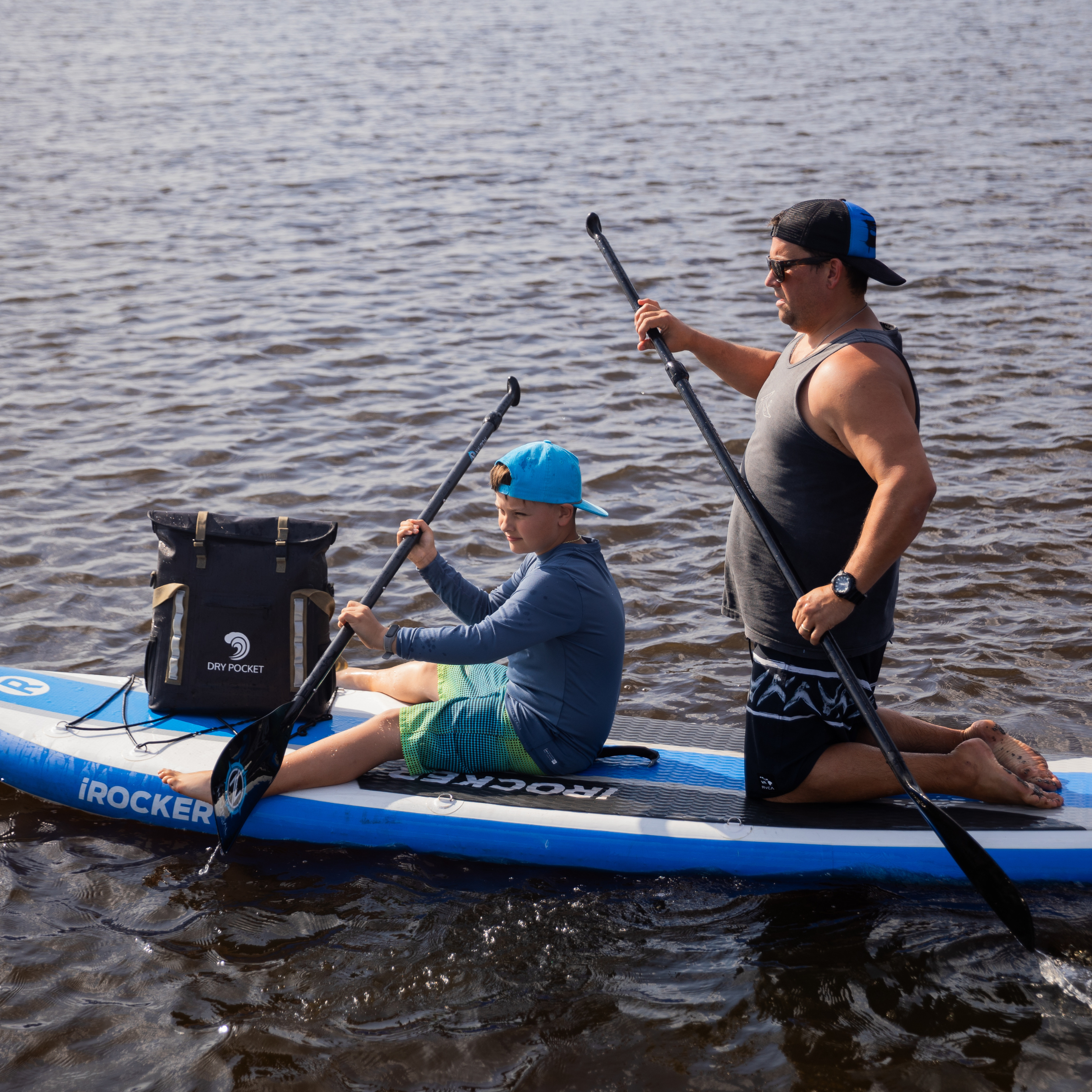 iROCKER inflatable paddle board with dry bag, used by man and boy on water for outdoor recreation