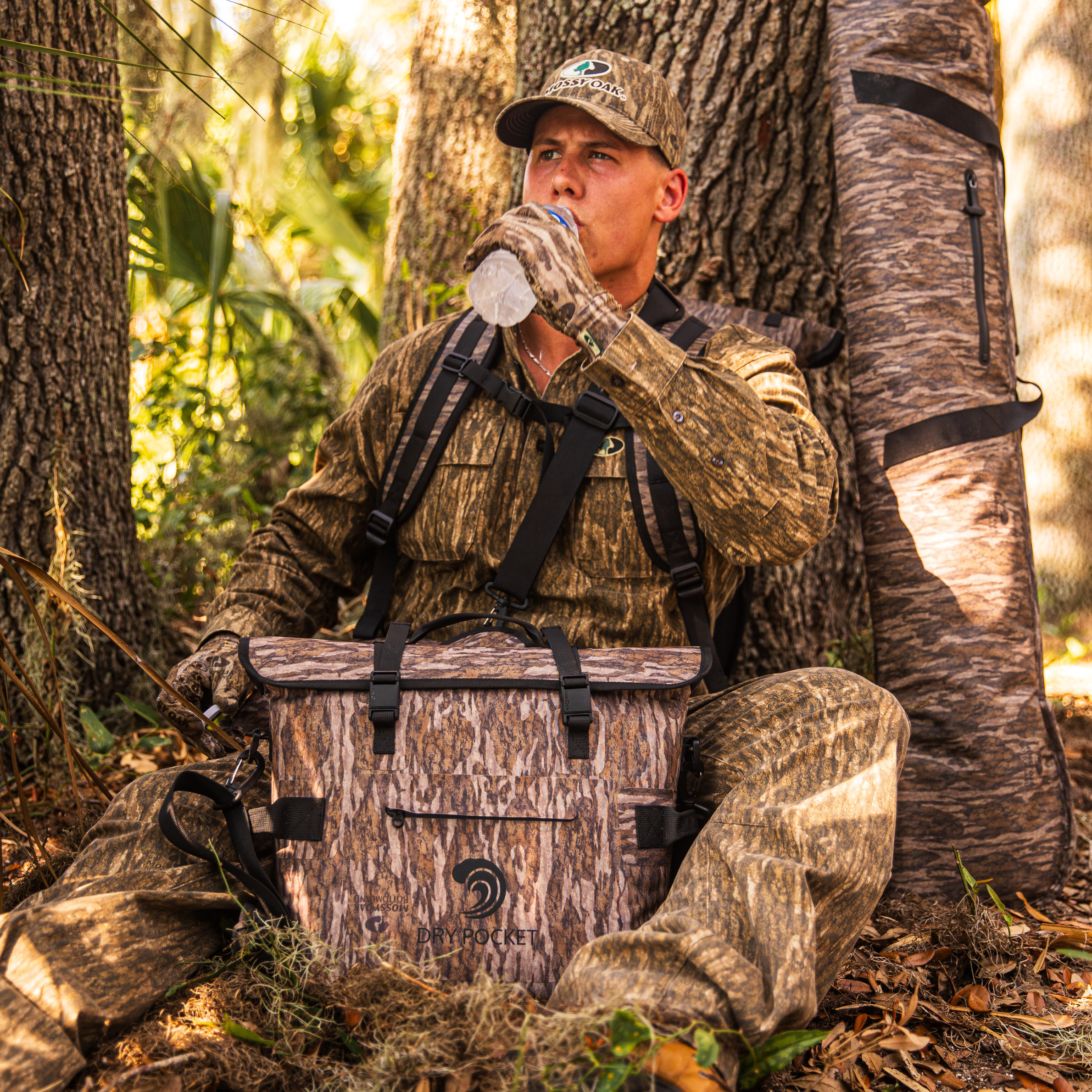 Mossy Oak camo dry pocket bag for hunting, worn by hunter in forest with water bottle and gear