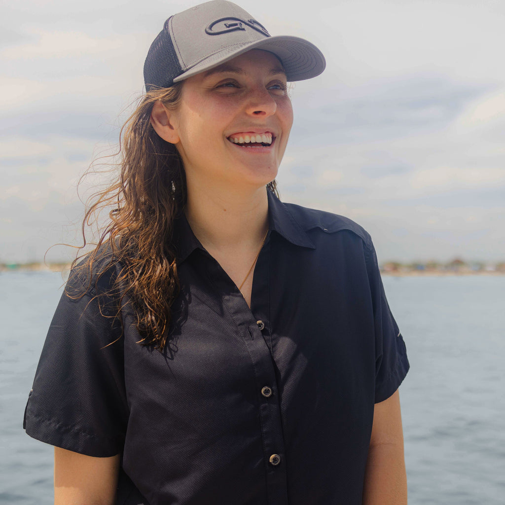 Woman wearing gray and navy trucker hat with logo, ideal for fishing or outdoor adventures near water
