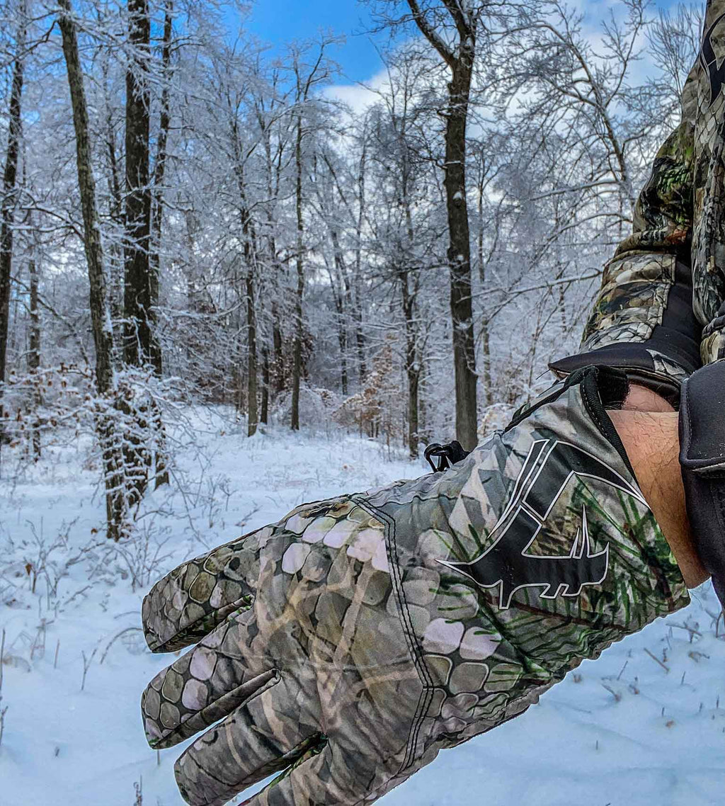 Hunter wearing Vycah Conley insulated camo gloves in snow-covered winter timber