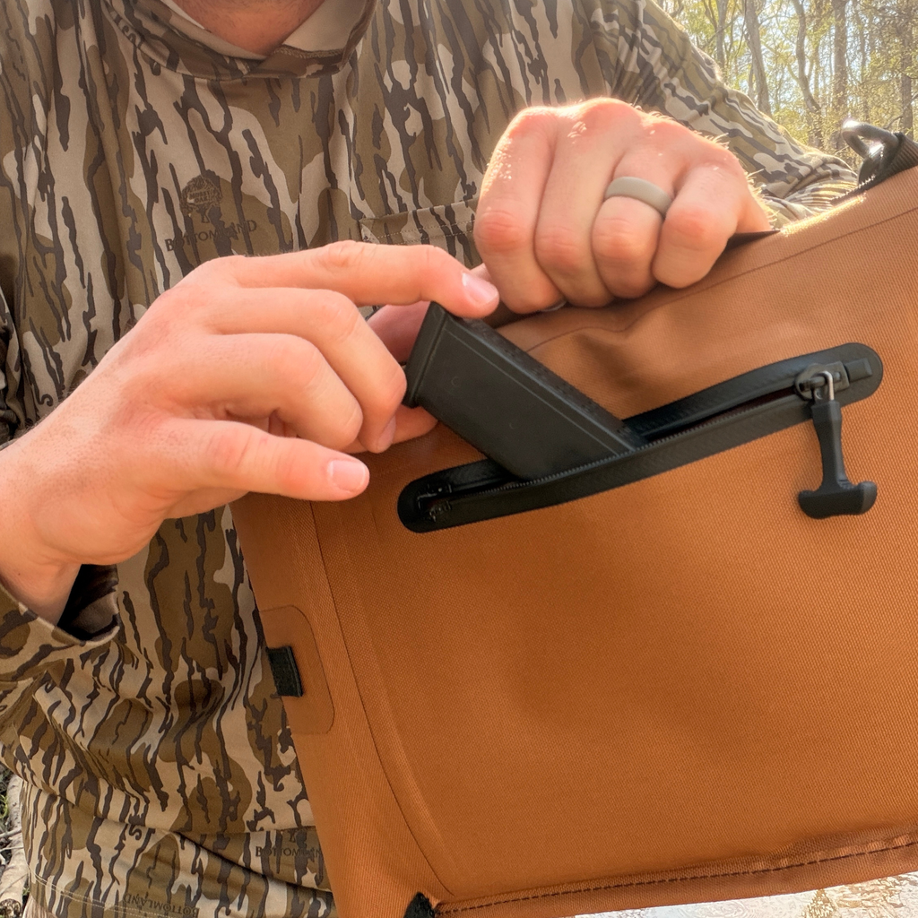 Hunter in camo accessing gear from tan outdoor pack with zipper pocket