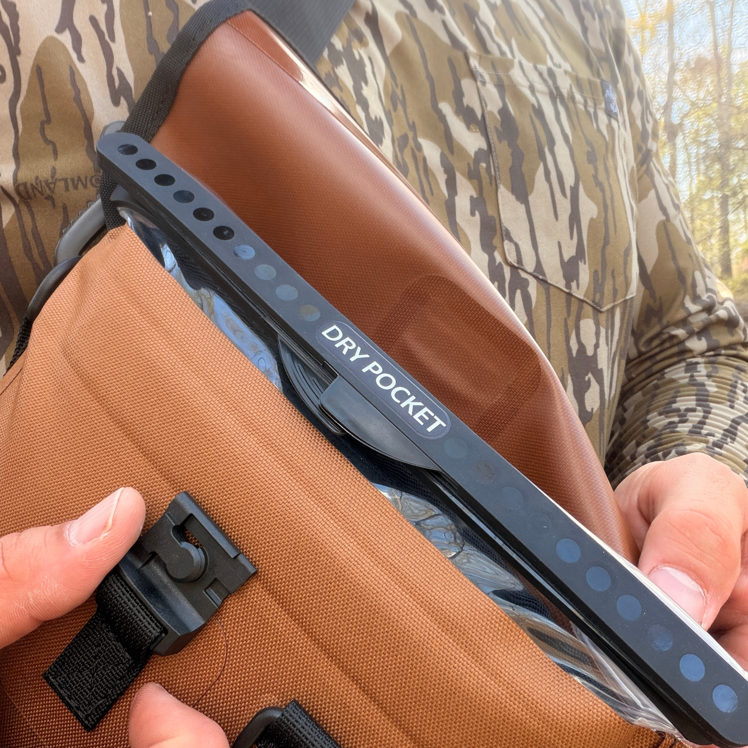 Brown tactical dry pocket pouch with black strap, shown on camo hunting gear for outdoor use.