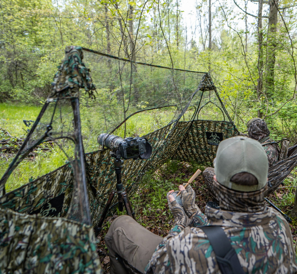 Camo hunting blind with photographer in forest, using camera on tripod for wildlife observation