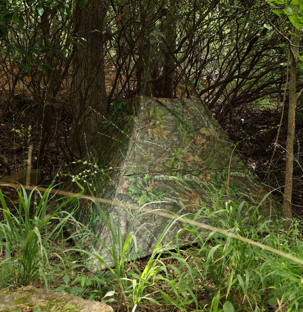 Camo hunting blind with leaf and bark pattern, blending into forest underbrush for stealthy wildlife observation.